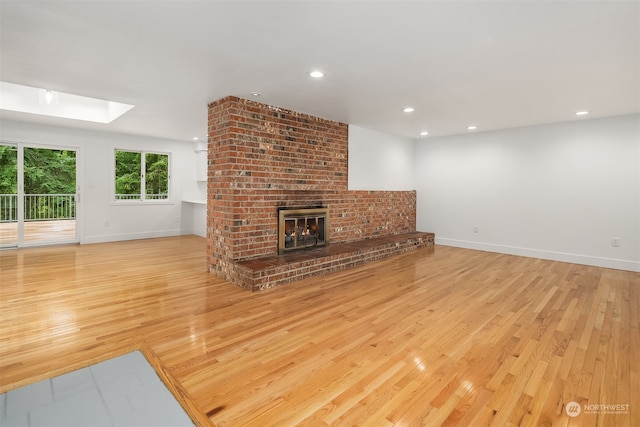 living room featuring brick wall, a skylight, light hardwood / wood-style floors, and a brick fireplace