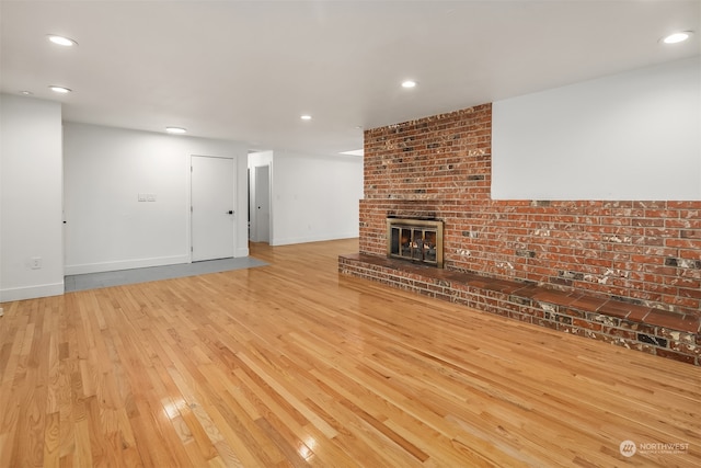 unfurnished living room with a fireplace, brick wall, and light hardwood / wood-style flooring