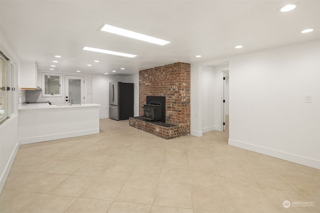 unfurnished living room with light tile patterned floors, a wood stove, a brick fireplace, and brick wall