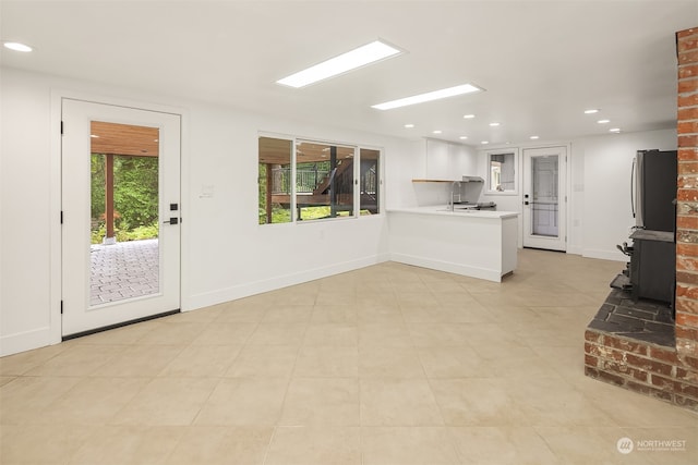 unfurnished living room featuring a wood stove, a wealth of natural light, and light tile patterned flooring