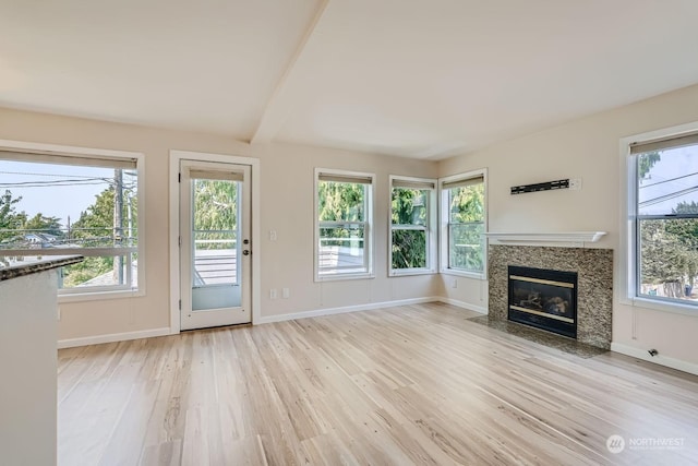 unfurnished living room with a premium fireplace, vaulted ceiling with beams, and light wood-type flooring