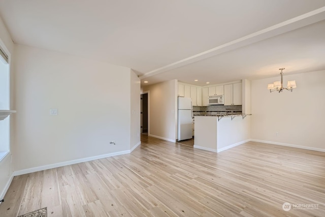 unfurnished living room featuring a chandelier and light hardwood / wood-style flooring