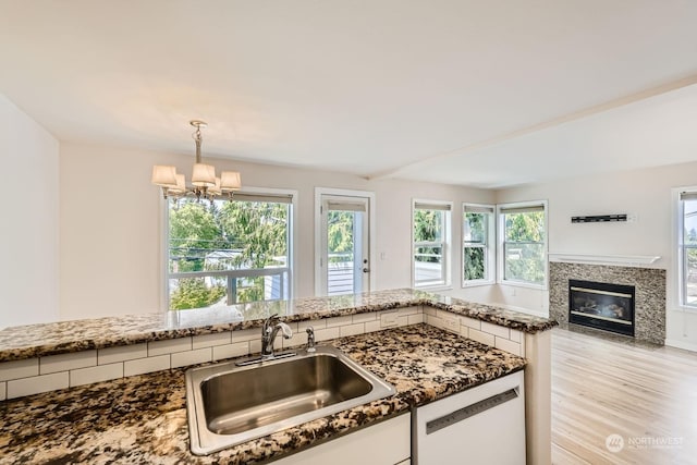 kitchen featuring dishwashing machine, sink, pendant lighting, light hardwood / wood-style flooring, and dark stone counters