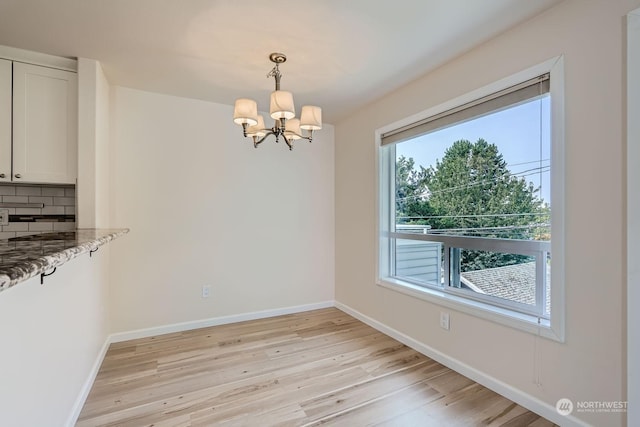 unfurnished dining area featuring an inviting chandelier and light hardwood / wood-style flooring