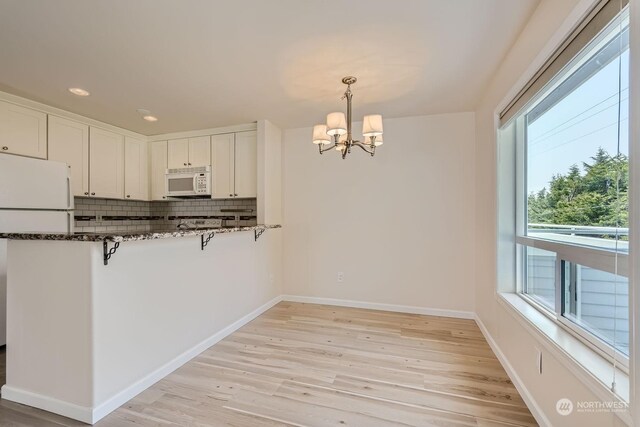 kitchen featuring a breakfast bar, white cabinetry, tasteful backsplash, pendant lighting, and white appliances