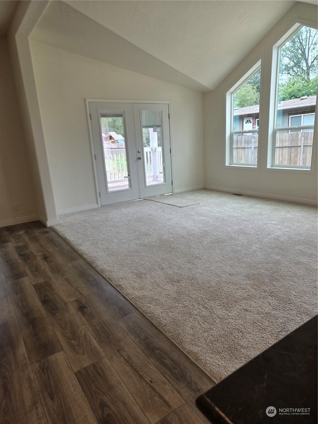 unfurnished living room featuring baseboards, dark wood-type flooring, dark colored carpet, vaulted ceiling, and french doors