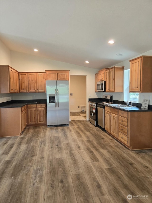 kitchen with vaulted ceiling, appliances with stainless steel finishes, dark countertops, and a sink