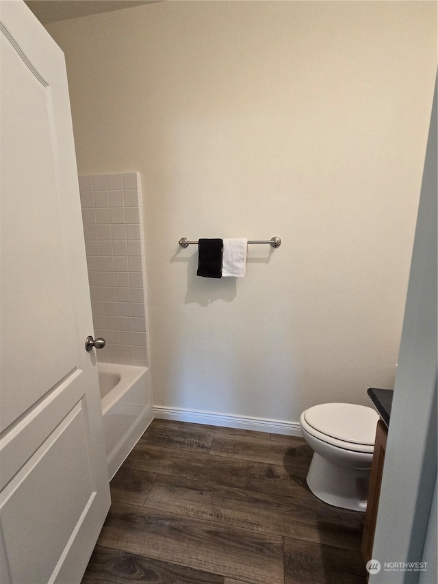 bathroom featuring a bathing tub, wood finished floors, toilet, and baseboards