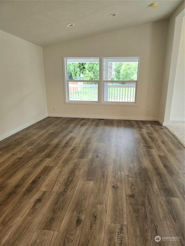 unfurnished room featuring dark wood-style floors, vaulted ceiling, and plenty of natural light