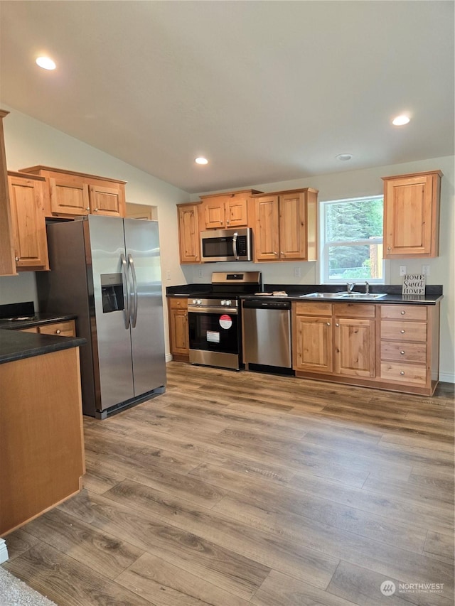 kitchen with dark countertops, lofted ceiling, recessed lighting, light wood-style flooring, and appliances with stainless steel finishes