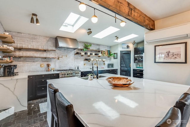 kitchen with pendant lighting, wall chimney range hood, sink, a wall unit AC, and light stone counters