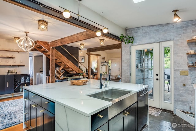 kitchen with brick wall, an island with sink, dishwasher, hanging light fixtures, and light stone countertops