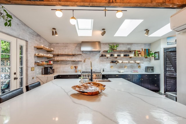 kitchen featuring pendant lighting, a wall mounted air conditioner, light stone countertops, and wall chimney range hood