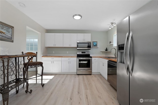 kitchen with sink, light wood-type flooring, white cabinets, and appliances with stainless steel finishes