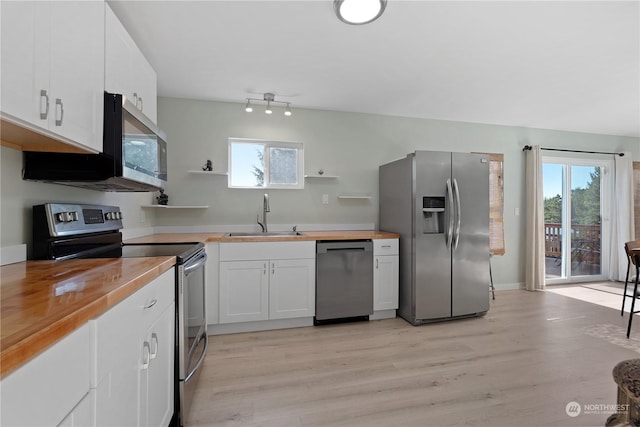 kitchen featuring sink, white cabinetry, stainless steel appliances, a wealth of natural light, and wood counters