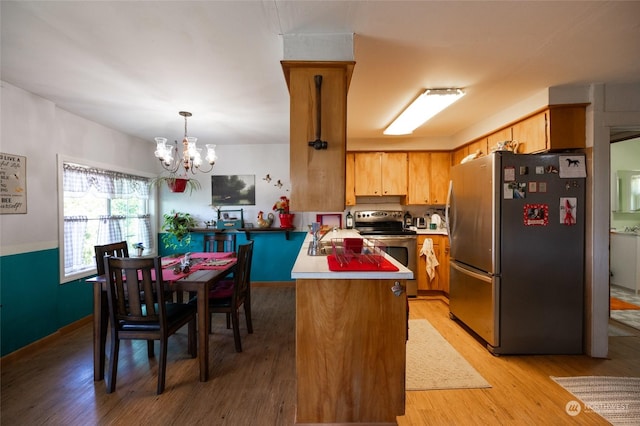 kitchen featuring appliances with stainless steel finishes, a chandelier, hanging light fixtures, kitchen peninsula, and light wood-type flooring