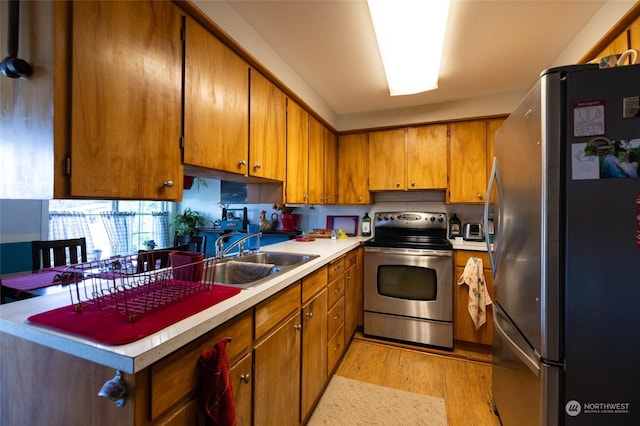 kitchen with appliances with stainless steel finishes, sink, and light wood-type flooring