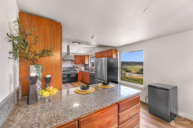 kitchen with light hardwood / wood-style flooring, backsplash, wall chimney exhaust hood, sink, and stainless steel appliances