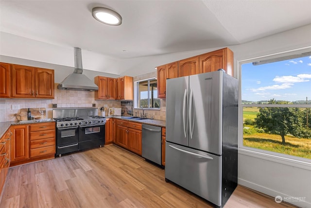 kitchen with lofted ceiling, stainless steel appliances, a sink, wall chimney exhaust hood, and brown cabinetry