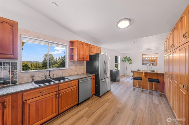 kitchen featuring brown cabinets, decorative backsplash, appliances with stainless steel finishes, light wood-style floors, and a sink