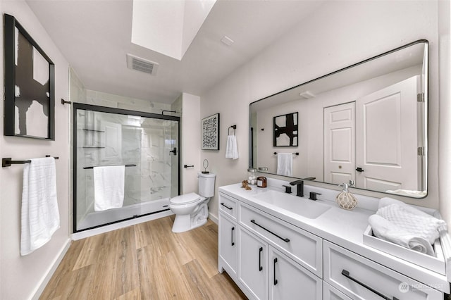 bathroom with visible vents, toilet, a stall shower, vanity, and wood finished floors