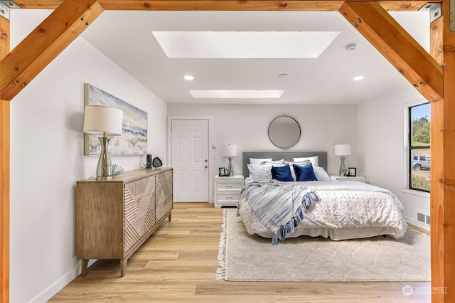 bedroom with beam ceiling, light hardwood / wood-style floors, and a skylight