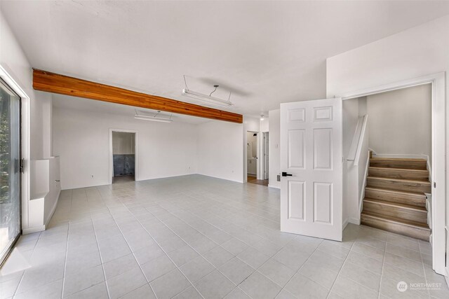 empty room with light tile patterned floors, beamed ceiling, and stairway