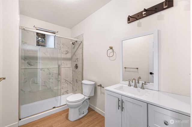 full bathroom featuring toilet, wood finished floors, vanity, baseboards, and a marble finish shower