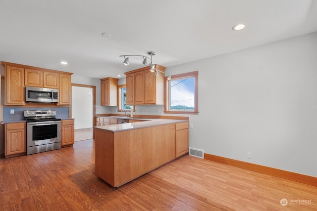 kitchen featuring appliances with stainless steel finishes, kitchen peninsula, sink, and light wood-type flooring