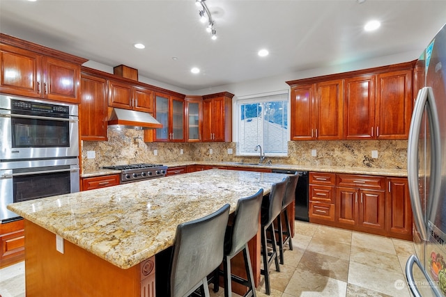 kitchen with premium range hood, a kitchen island, appliances with stainless steel finishes, sink, and light stone counters