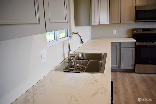 kitchen with sink, light stone counters, stainless steel electric range oven, light hardwood / wood-style flooring, and gray cabinetry