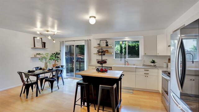 kitchen with white cabinets, light wood-type flooring, sink, a center island, and appliances with stainless steel finishes