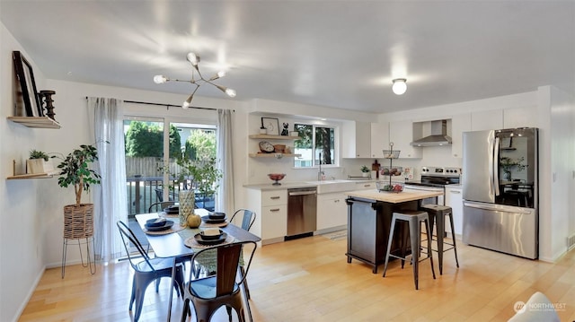 kitchen with white cabinetry, light wood-type flooring, wall chimney exhaust hood, a center island, and appliances with stainless steel finishes