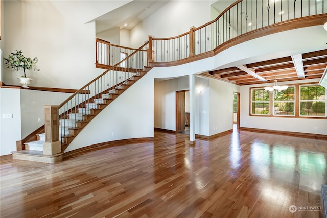 unfurnished living room with beam ceiling, a notable chandelier, and hardwood / wood-style flooring