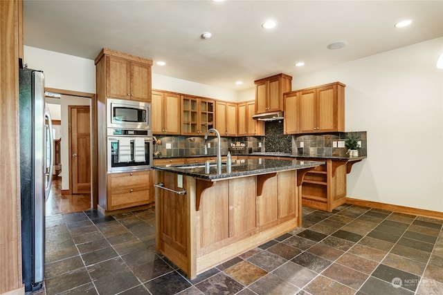 kitchen featuring a kitchen bar, stainless steel appliances, sink, and dark stone countertops