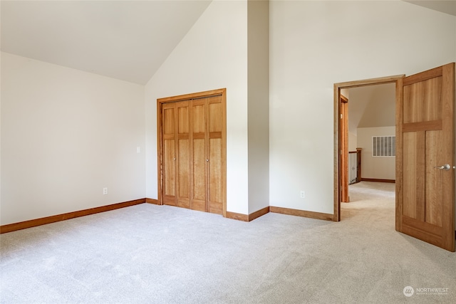 unfurnished bedroom featuring high vaulted ceiling, a closet, and light colored carpet