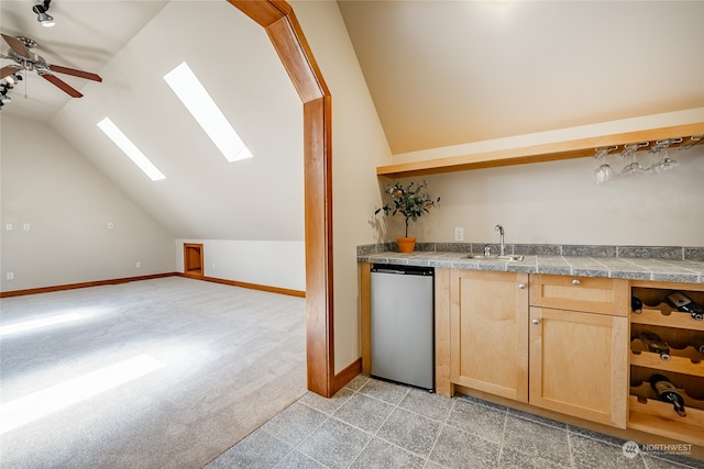 interior space featuring light brown cabinets, stainless steel dishwasher, vaulted ceiling with skylight, ceiling fan, and sink