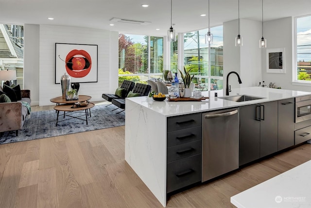 kitchen featuring stainless steel appliances, sink, hanging light fixtures, light wood-type flooring, and an island with sink