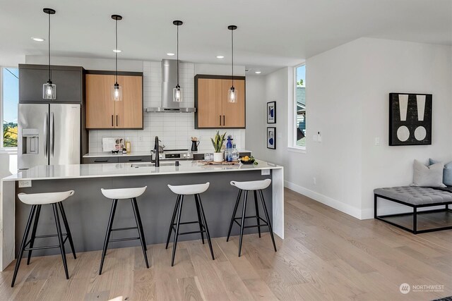 kitchen featuring stainless steel fridge with ice dispenser, light hardwood / wood-style flooring, tasteful backsplash, and wall chimney range hood