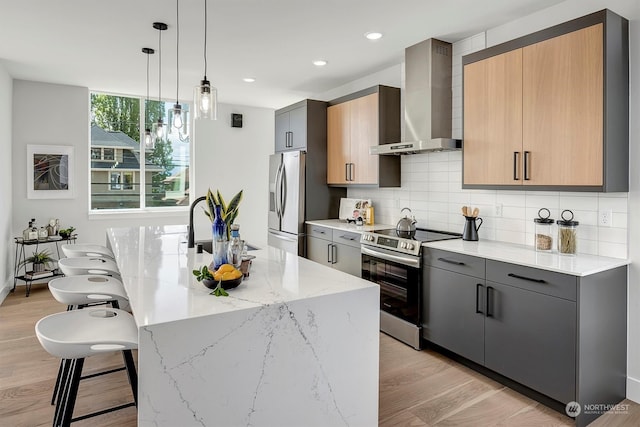 kitchen featuring stainless steel appliances, light stone counters, light wood-type flooring, and wall chimney range hood