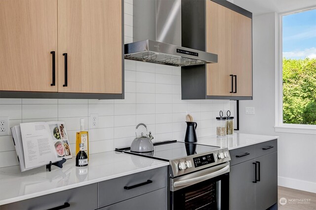 kitchen with stainless steel range with electric stovetop, light stone countertops, tasteful backsplash, and wall chimney exhaust hood