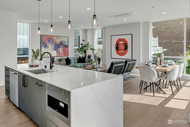 kitchen with light hardwood / wood-style flooring, sink, light stone counters, decorative light fixtures, and a kitchen island with sink