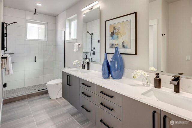 bathroom with tile patterned floors, a shower with door, toilet, and dual bowl vanity