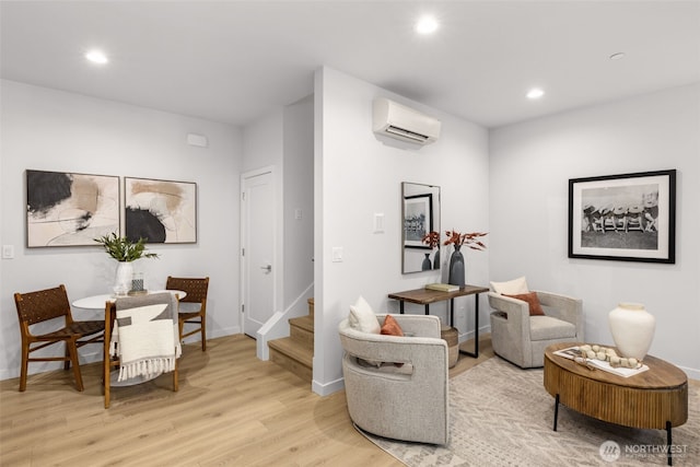 sitting room with recessed lighting, light wood-type flooring, a wall mounted air conditioner, baseboards, and stairs