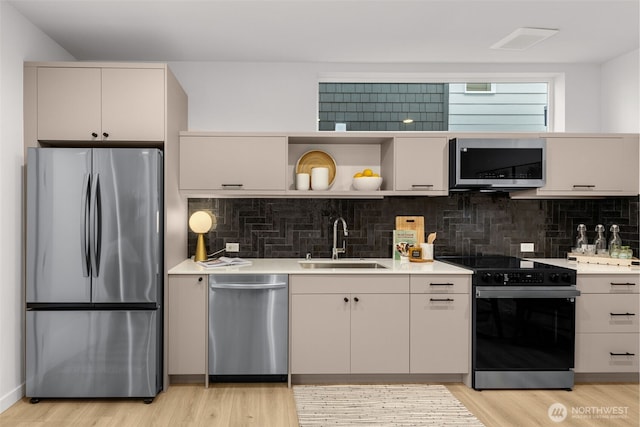 kitchen featuring appliances with stainless steel finishes, light countertops, a sink, and light wood-style flooring