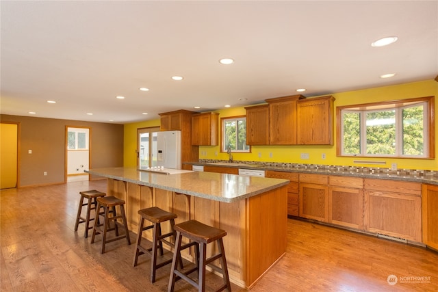 kitchen with a center island, light hardwood / wood-style flooring, white appliances, and a kitchen bar