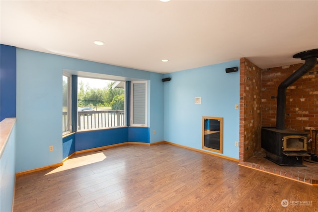 unfurnished living room with brick wall, a wood stove, and wood-type flooring