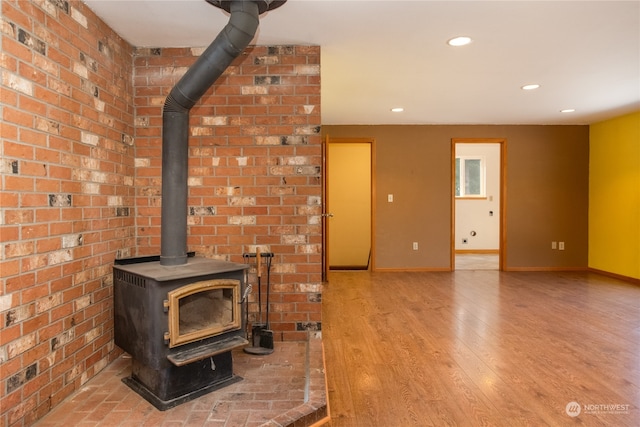 unfurnished living room featuring brick wall, hardwood / wood-style flooring, and a wood stove