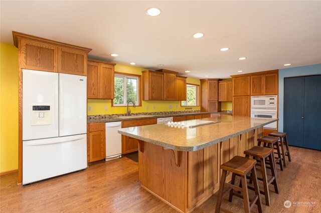 kitchen featuring hardwood / wood-style floors, white appliances, sink, a kitchen bar, and a kitchen island