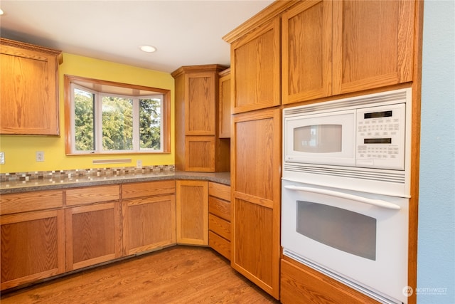 kitchen with wall oven, dark stone counters, light hardwood / wood-style flooring, and white microwave